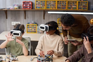 テーブルに座ってVRメガネにロボットを投影し、ロボット工学の授業中に教師が彼らを支援する子供たちのグループ