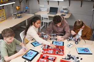 Gruppo di studenti seduti al tavolo con computer e robot di costruzione dal costruttore secondo il progetto alla lezione di robotica