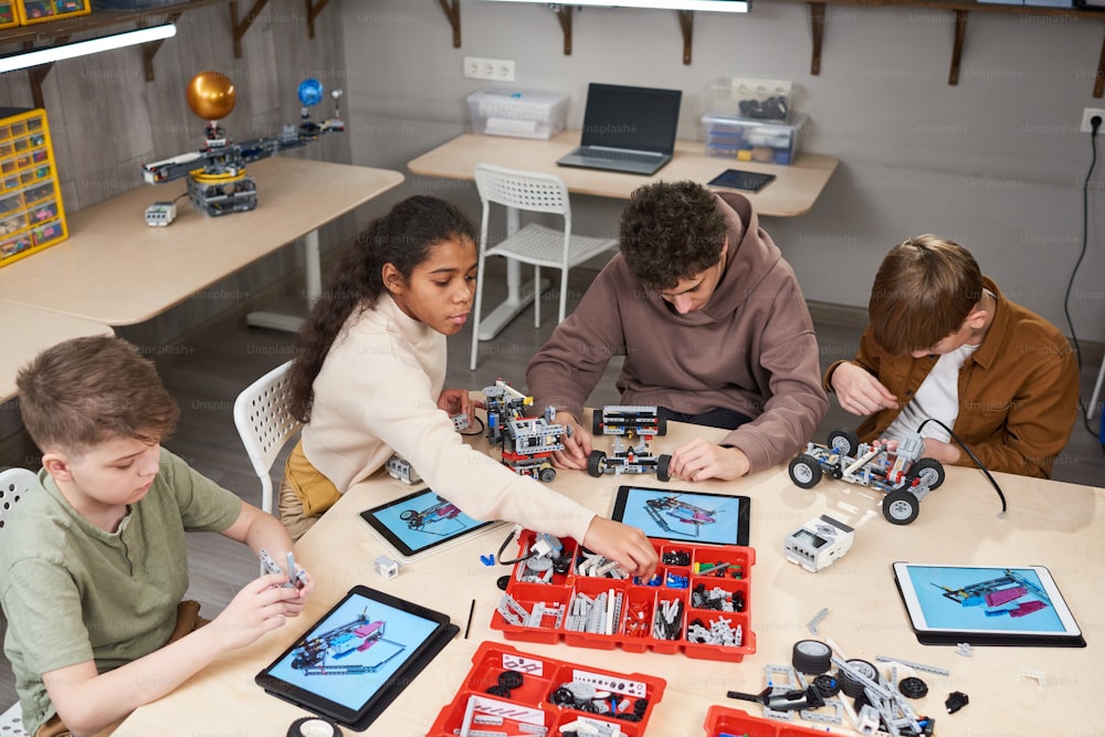 Grupo de alunos sentados à mesa com computadores e construindo robôs do construtor de acordo com o projeto na aula de robótica