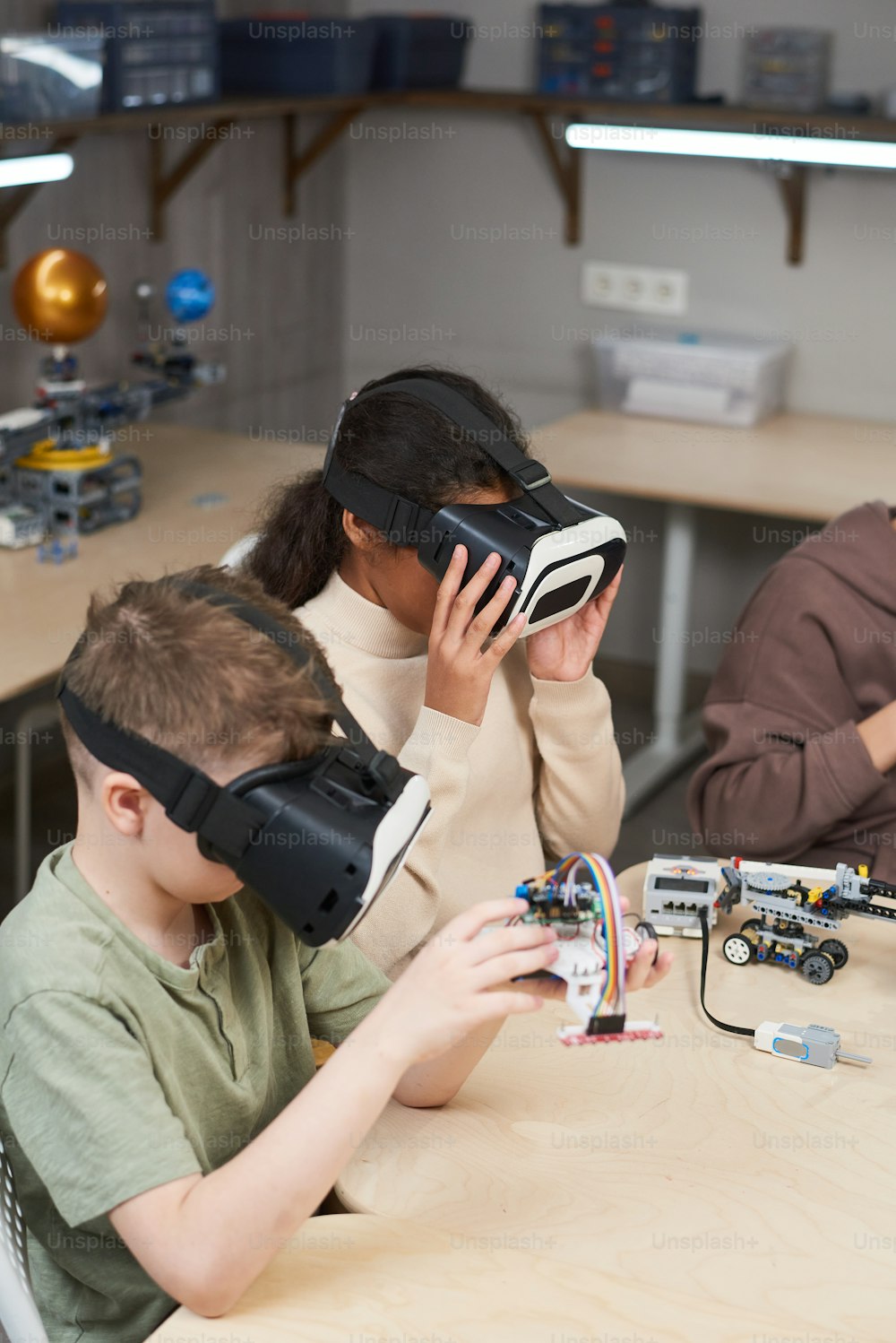 Children projecting robots in virtual reality glasses at the table during robotics lesson
