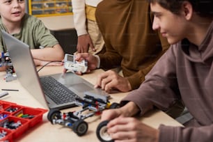 Close-up of teenagers using laptop at the table during their teamwork at robotics lesson