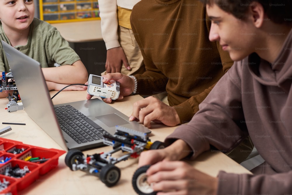 Primo piano di adolescenti che usano il laptop al tavolo durante il loro lavoro di squadra a lezione di robotica