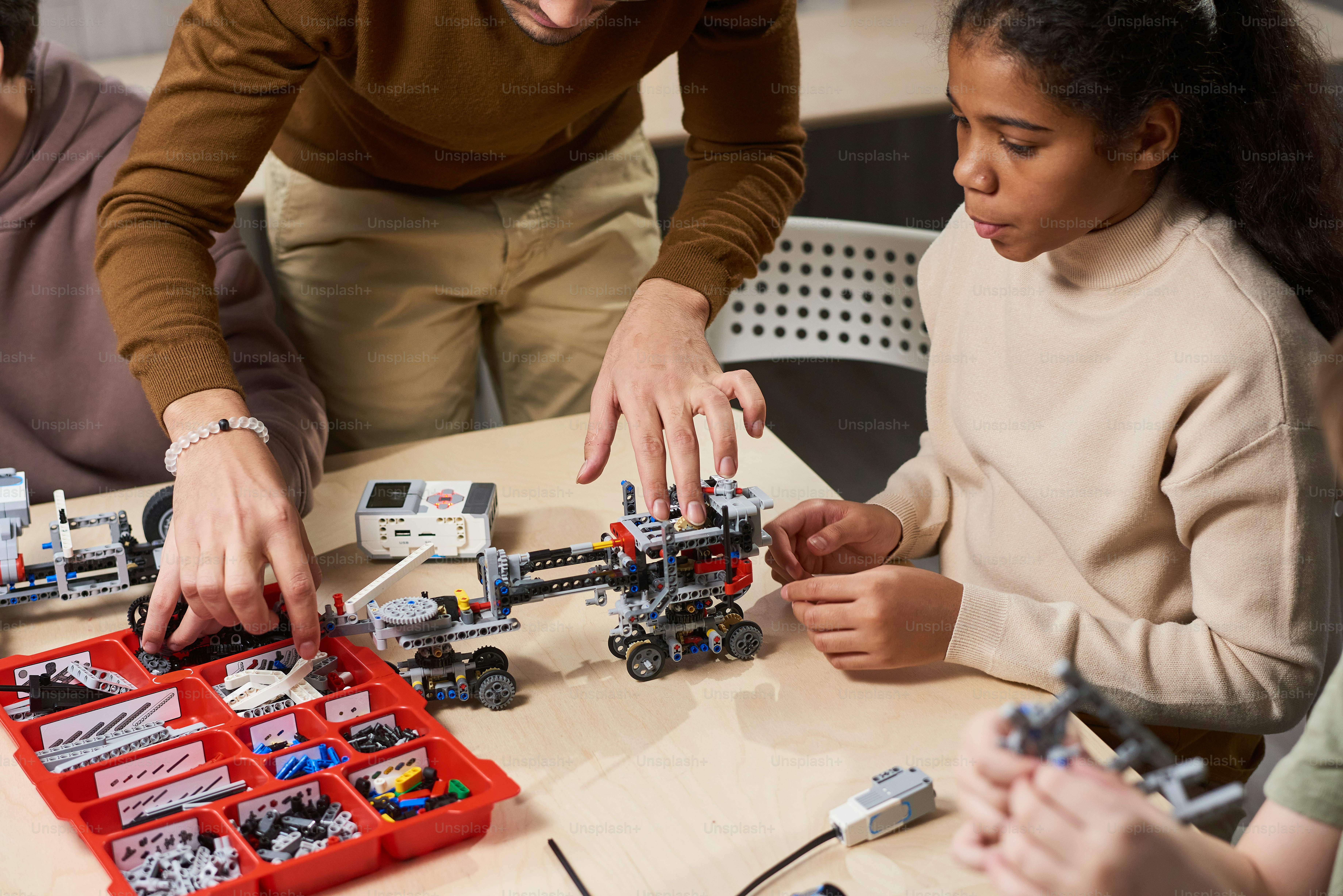 African teenage girl watching for building the robot by the teacher while sitting at the table at science lesson