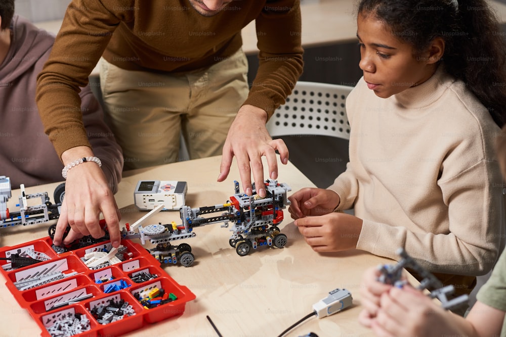 과학 수업에서 테이블에 앉아 있는 동안 교사가 로봇을 만드는 것을 지켜보는 아프리카 십대 소녀