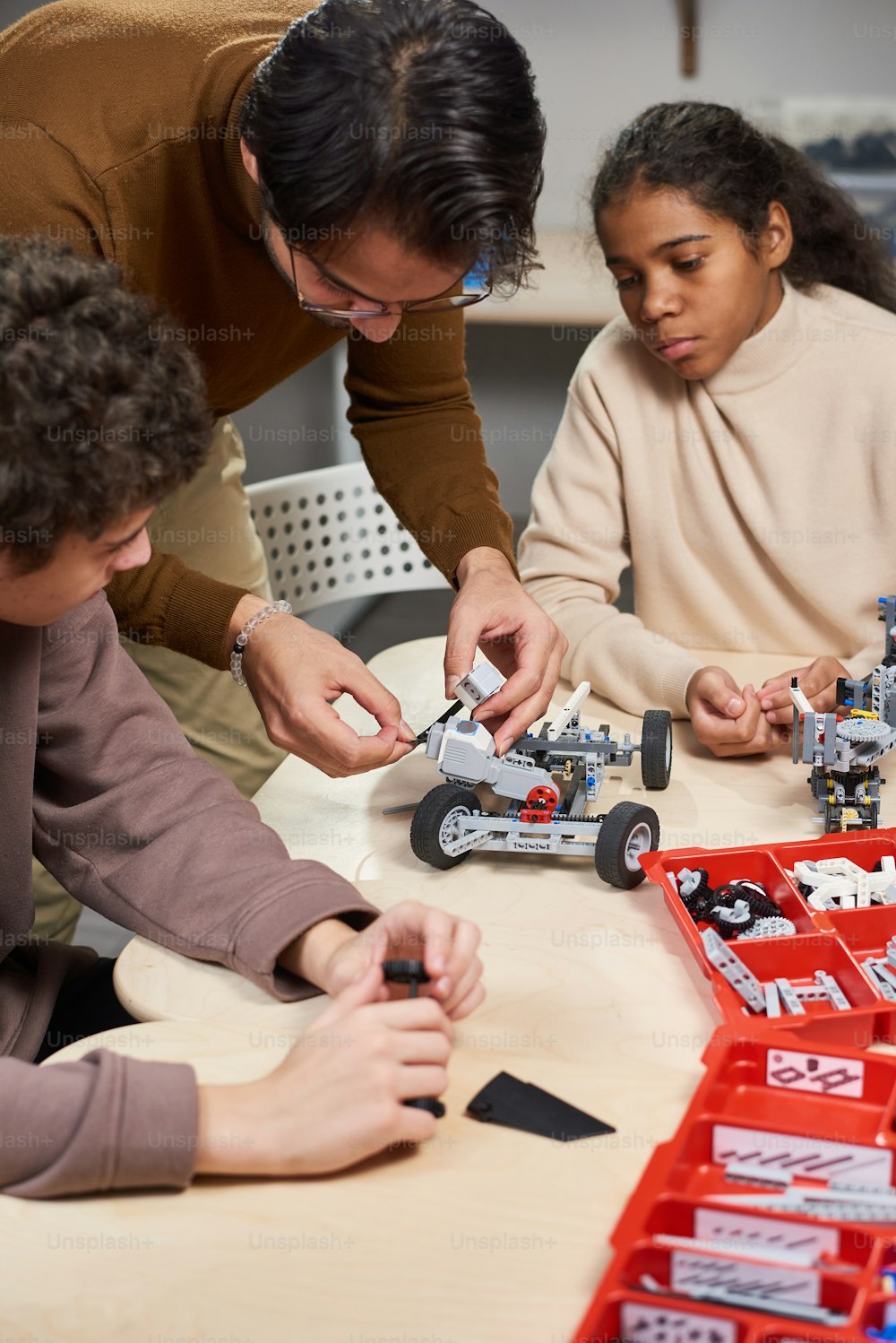 Jovem professor mostrando às crianças como construir o carro robô na mesa durante a aula de engenharia