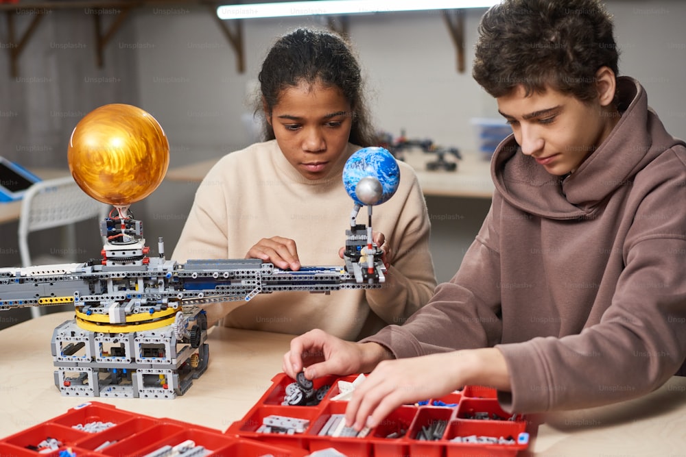 Garçon et fille programmant des jouets électriques à table pendant leur cours à l’école de sciences