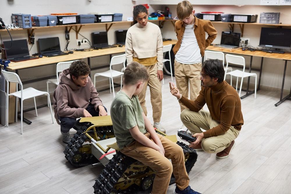 Giovane insegnante che spiega il lavoro della macchina robotica ai suoi studenti mentre lo esaminano durante la lezione di scienze