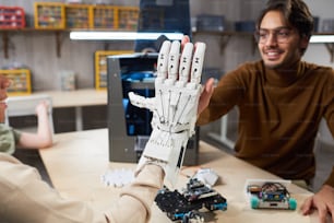 Student putting on the robotic arm on her hand and trying to control it, giving the high-five to her teacher during robotic lesson