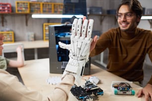 Aluna colocando o braço robótico em sua mão e tentando controlá-lo, dando o high-five para seu professor durante a aula de robótica