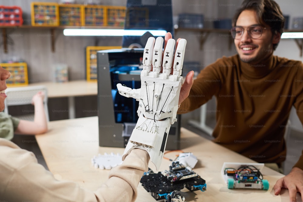 Estudiante poniendo el brazo robótico en su mano y tratando de controlarlo, dándole los cinco a su maestro durante la lección de robótica