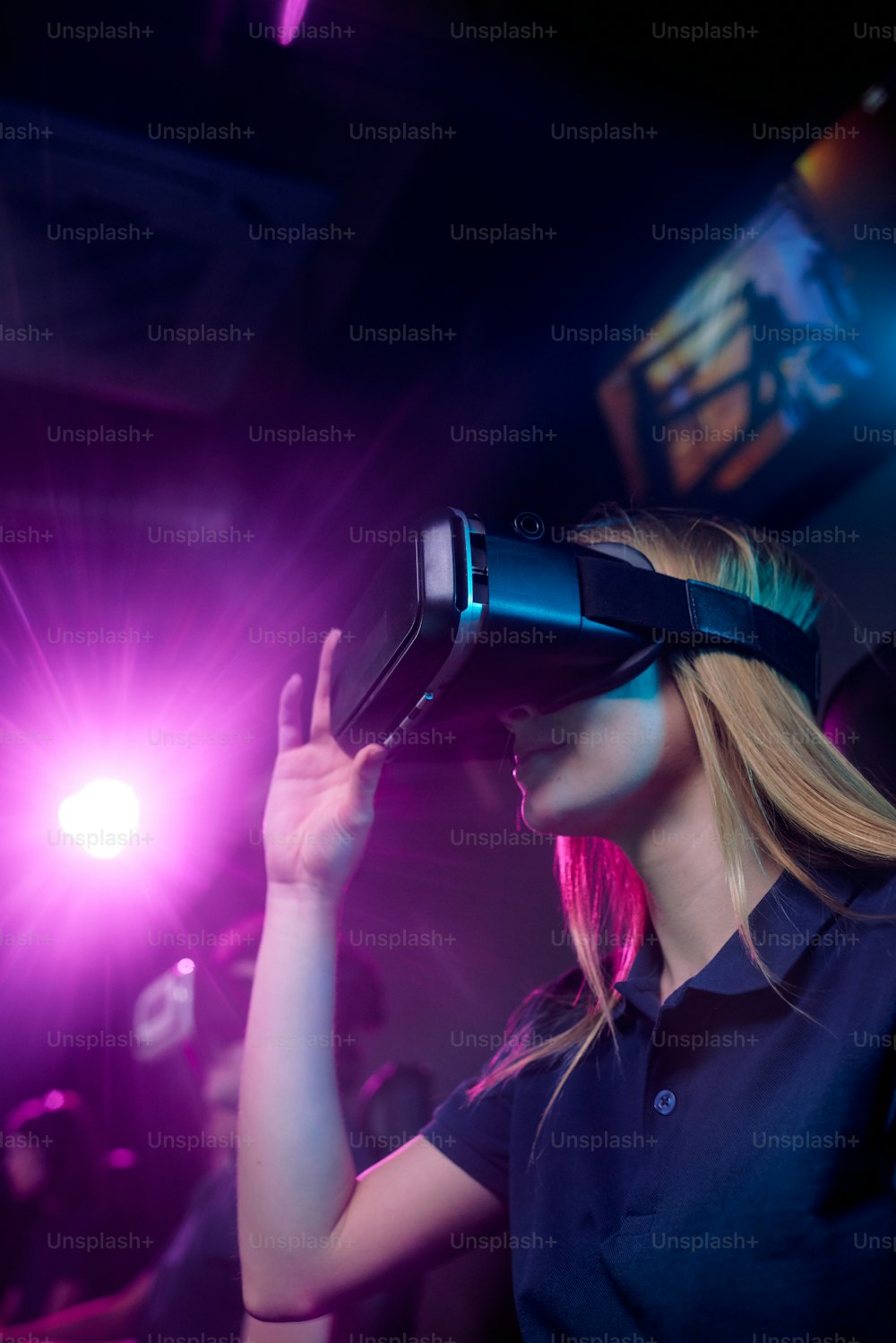 Mujer joven con auriculares de realidad 3D participando en una competencia de deportes cibernéticos mientras está sentada en un club de videojuegos contemporáneo con amigos