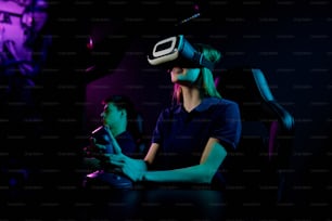 Chica sonriente en gafas de realidad virtual sentada en el sillón de los jugadores y usando el mango del joystick mientras juega al videojuego en el club de la computadora