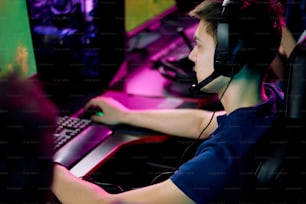 Ernster Junge mit Headset und Mikrofon sitzt am Tisch und spielt Videospiel im Computerclub
