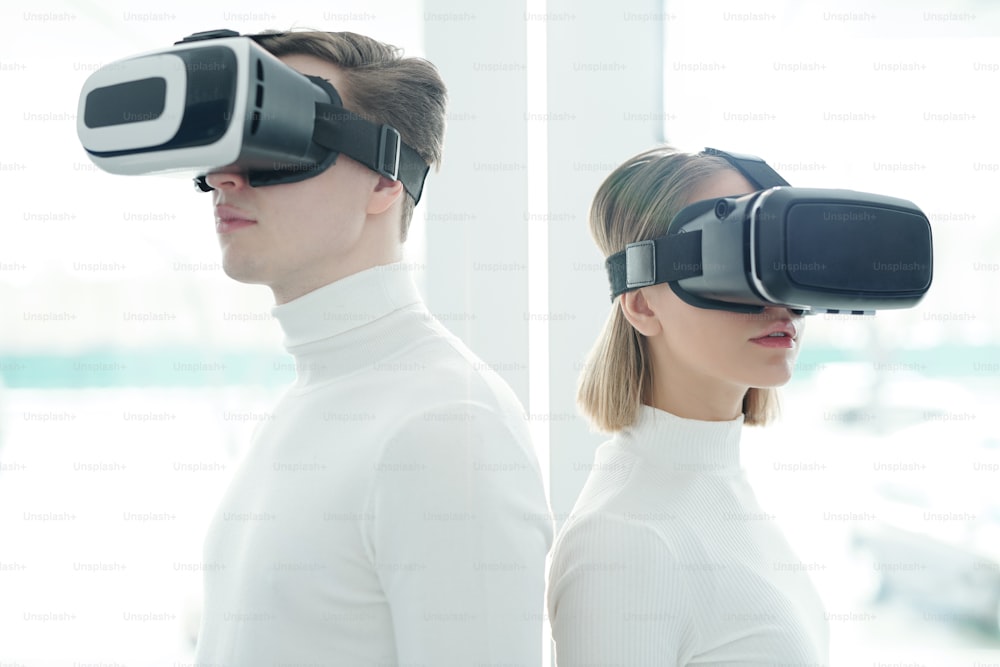 Junge Menschen in weißen Pullovern mit Virtual-Reality-Brillen, die Rücken an Rücken stehen