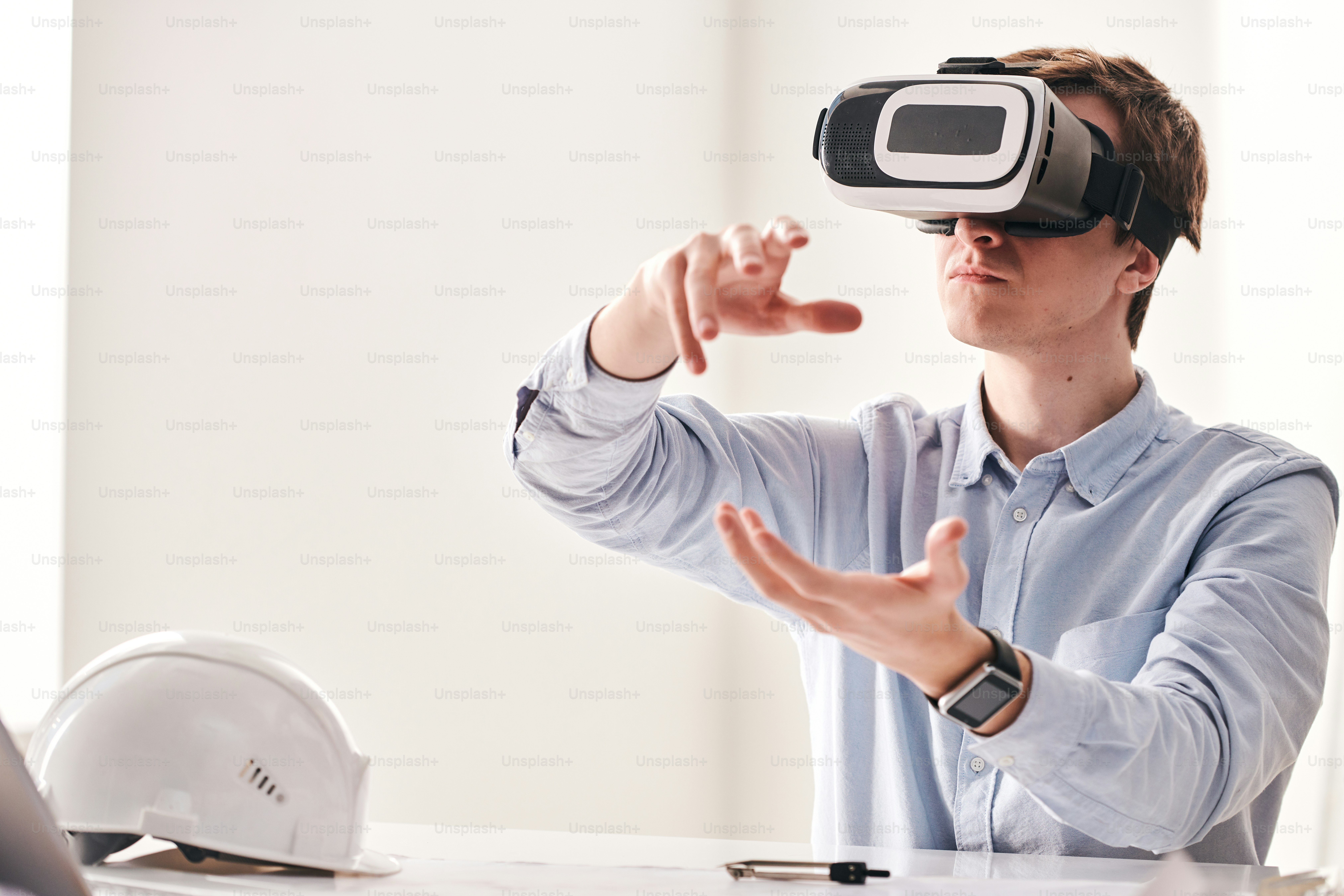 Busy young architect sitting at desk and gesturing hands while creating floor plan using virtual reality goggles