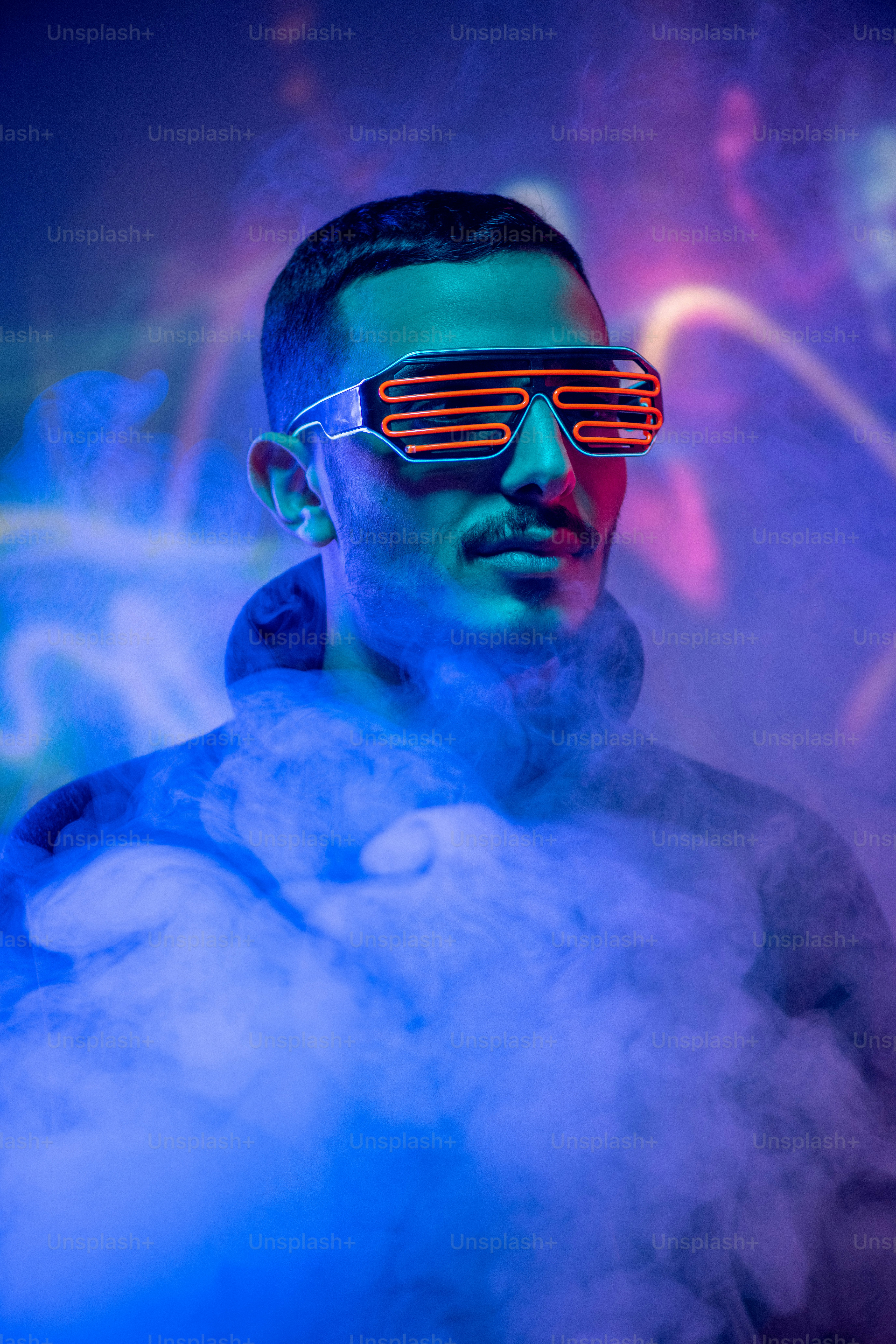 Head of contemporary young mixed-race man in red spiral eyewear among smoke and blue neon light