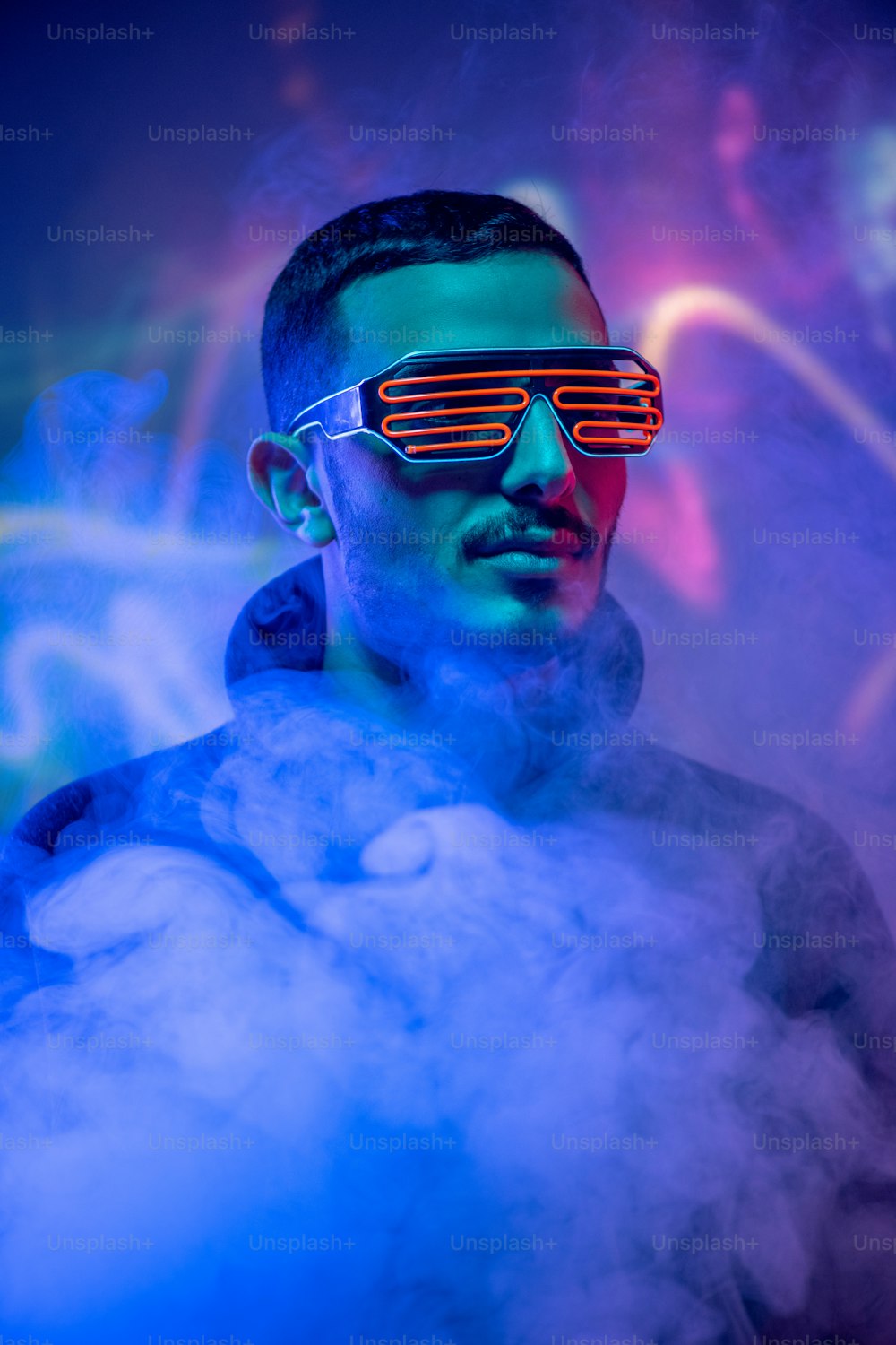 Cabeza de joven contemporáneo mestizo con gafas rojas en espiral entre humo y luz azul neón