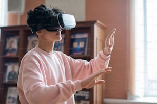 Mobile college student in casualwear and vr goggles touching virtual screen while moving in three dimensional reality