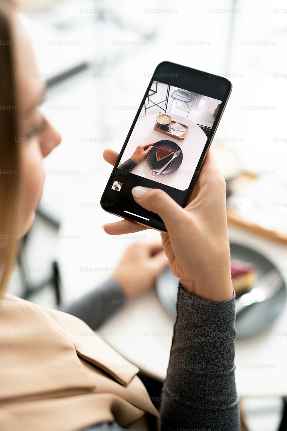Millennial feminino com smartphone tirando foto de cheesecake fresco apetitoso e xícara de cappuccino no café