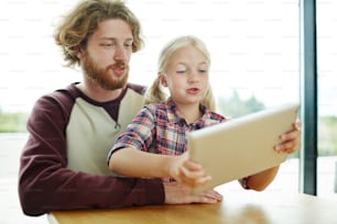 Menina bonita com touchpad e seu pai assistindo vídeo curioso on-line