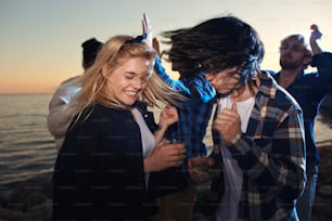 Young intercultural couple dancing by seaside with their friends on background