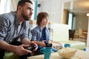 Serious man and little boy with consoles watching and playing video game