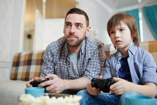 Man and little boy with joysticks looking at tv screen