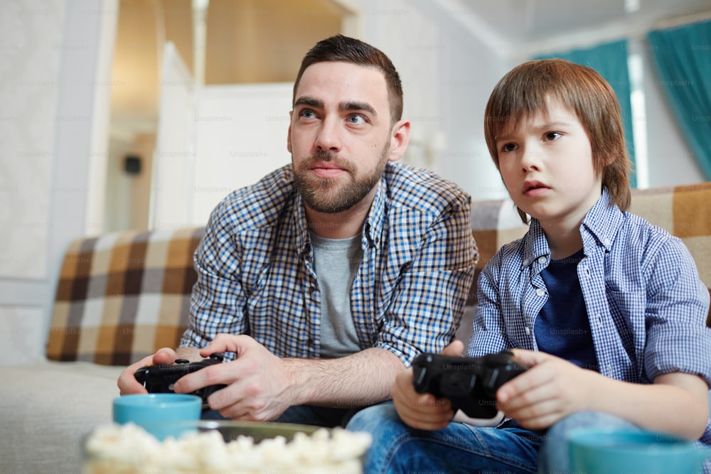 Hombre y niño pequeño con joysticks mirando la pantalla del televisor