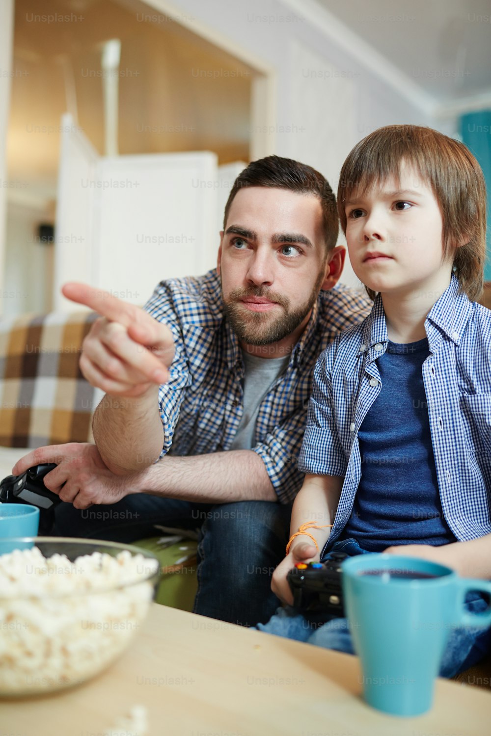 Father pointing at tv screen while gaming with his son at leisure