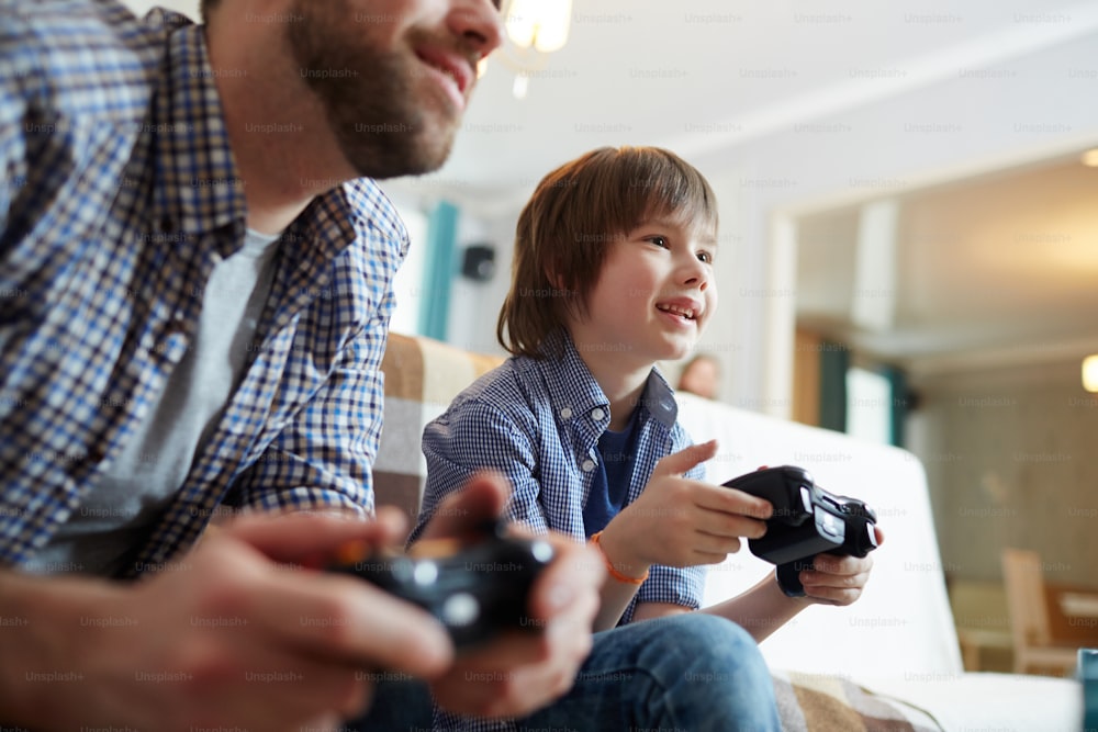 Niño feliz con consola y su padre jugando videojuegos en casa