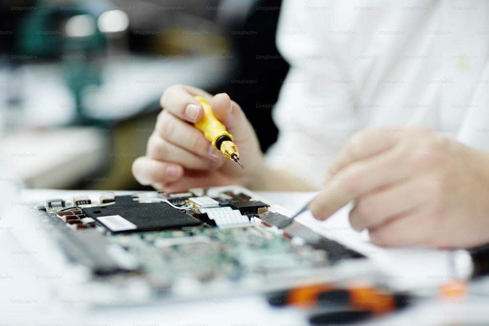 Closeup shot of unrecognizable man assembling circuit board using screwdriver and different tools on table in workshop
