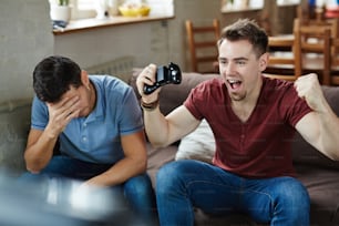 Ecstatic gameplayer expressing triumph with his defeated friend near by