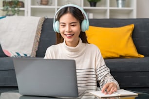 Cheerful beautiful Asian woman wearing headphones and using laptop at video calling meeting and study online on the Internet.