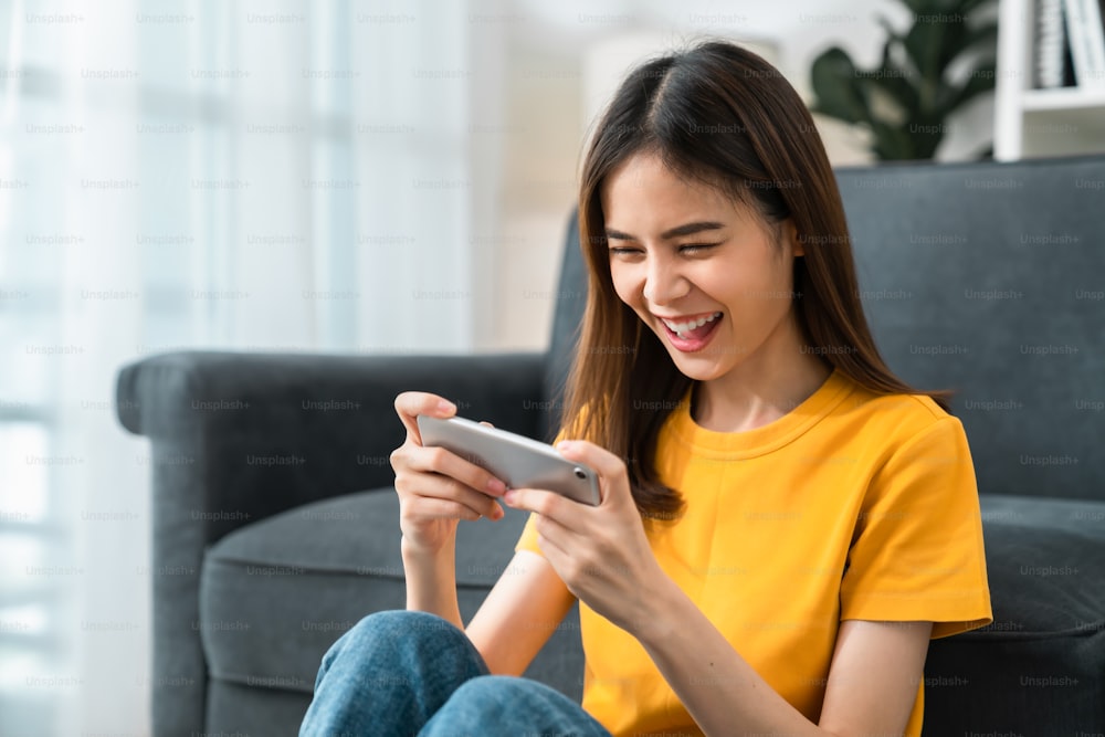 Emocionada joven asiática jugando un juego en línea en un teléfono inteligente.