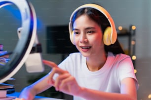 Lächelnde junge asiatische Frau mit Headset und Live-Übertragung im Internet und Lesen von Kommentaren mit Menschen in sozialen Medien auf dem Smartphone.