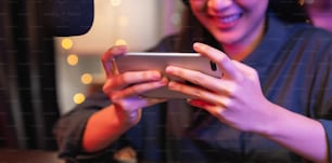 Mujer joven emocionada con auriculares y jugando un juego en línea en un teléfono inteligente con transmisión en vivo por Internet.