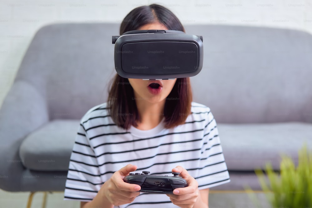 Aufgeregte junge asiatische Frau mit einem Virtual-Reality-Headset und Joysticks, Konzeptverbindung und Schnittstellen der digitalen Technologie.