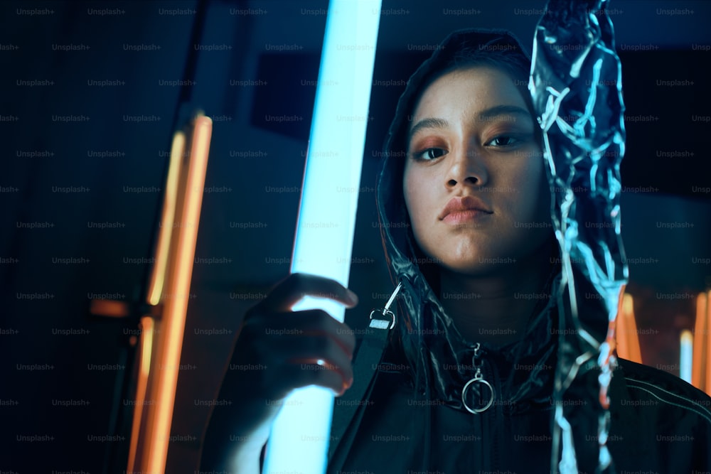 Futuristisches Porträt eines asiatischen Teenagers im Neonlicht. Sie ist ein serioses, gewagtes, modisches Cyberpunk-Mädchen