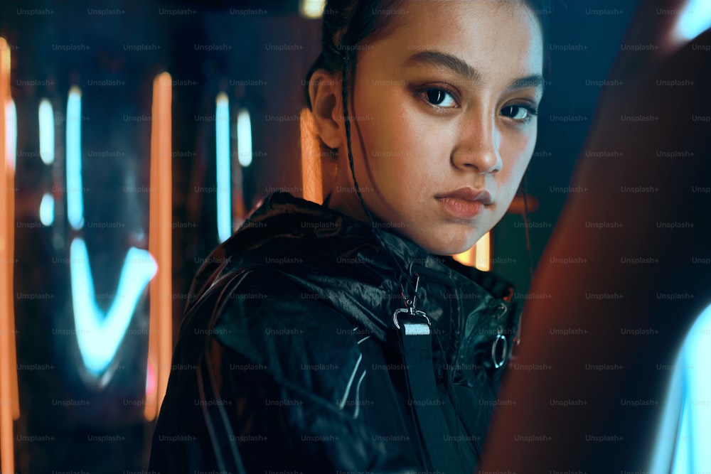 Ritratto futuristico di adolescente asiatico in luce al neon. È una ragazza alla moda seria, audace, cyberpunk