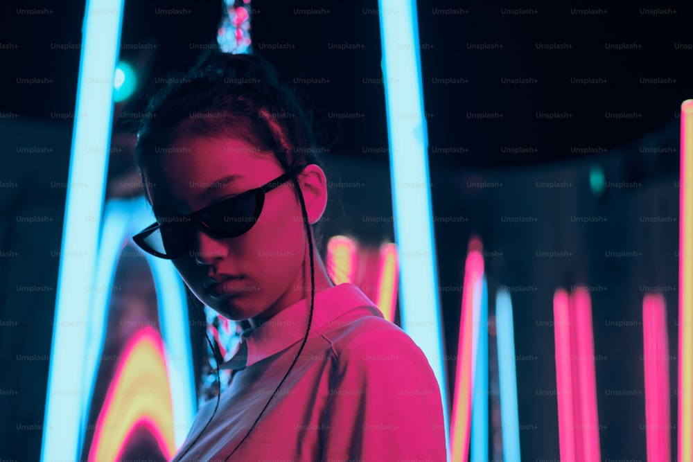 Porträt eines jungen asiatischen Teenager-Mädchens in stilvoller halbmondförmiger Sonnenbrille, in rotem und blauem Neonlicht. Cyber, futuristisches Porträtkonzept
