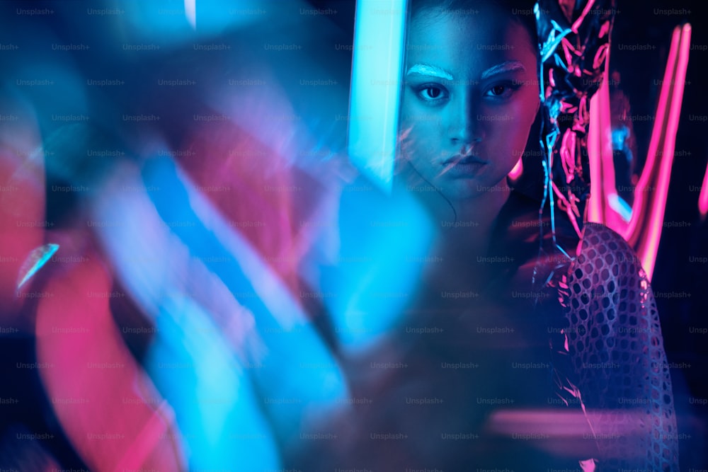 Futuristic portrait of asian teenager in neon light with sword like lamps. Neon smudged effects applied in front. She is seriour, daring, cyberpunk fashionable girl, in net clothes, white eyebrows