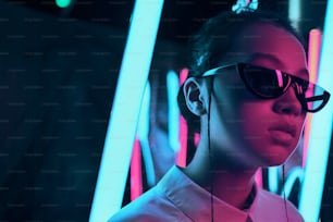 Portrait of young asian teenage girl in stylish crescent shaped sun glasses, in red anf blue neon light. Cyber, futuristic portrait concept