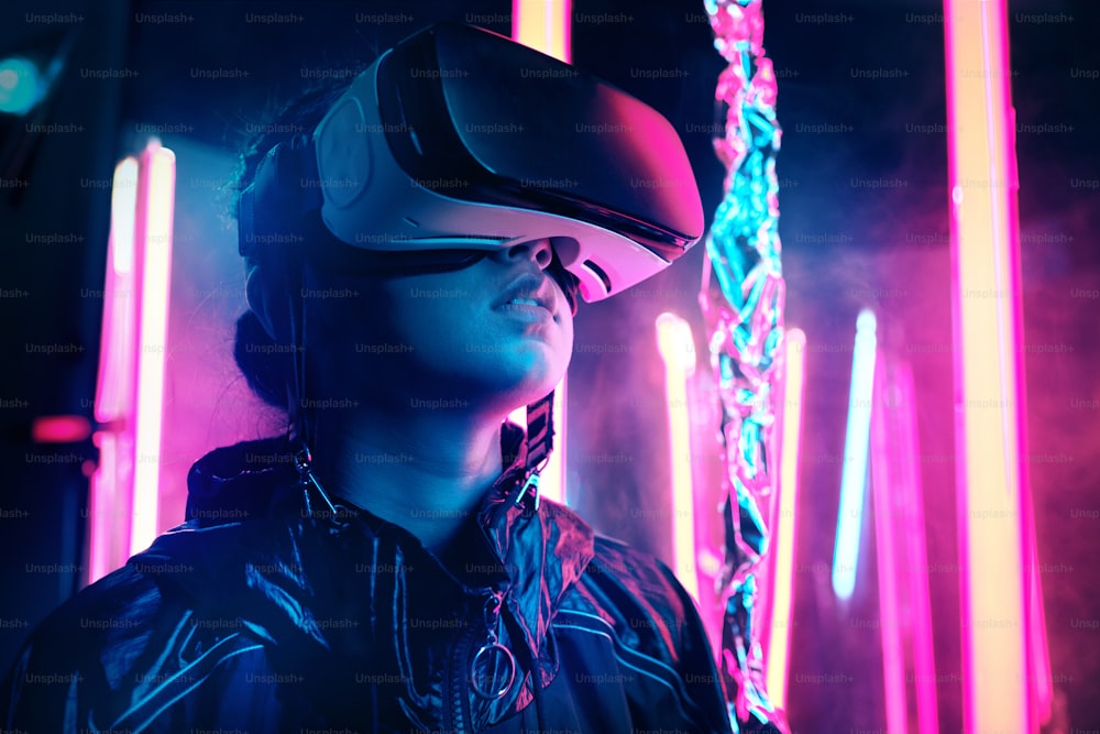 Portrait of young girl wearing Virtual Reality goggles. She is surrounded with neon light. Virtual Reality Point of View concept