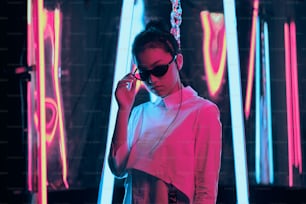 Retrato de una joven adolescente asiática con elegantes gafas de sol en forma de media luna, en luz de neón roja y azul. Concepto de retrato ciber y futurista