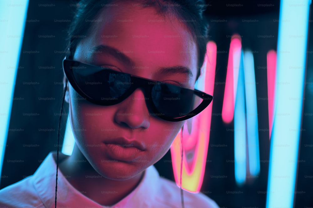 세련된 초승달 모양의 선글라스를 쓴 젊은 아시아 십대 소녀의 초상화, 빨간색과 파란색 네온 불빛. 사이버, 미래 지향적인 초상화 개념