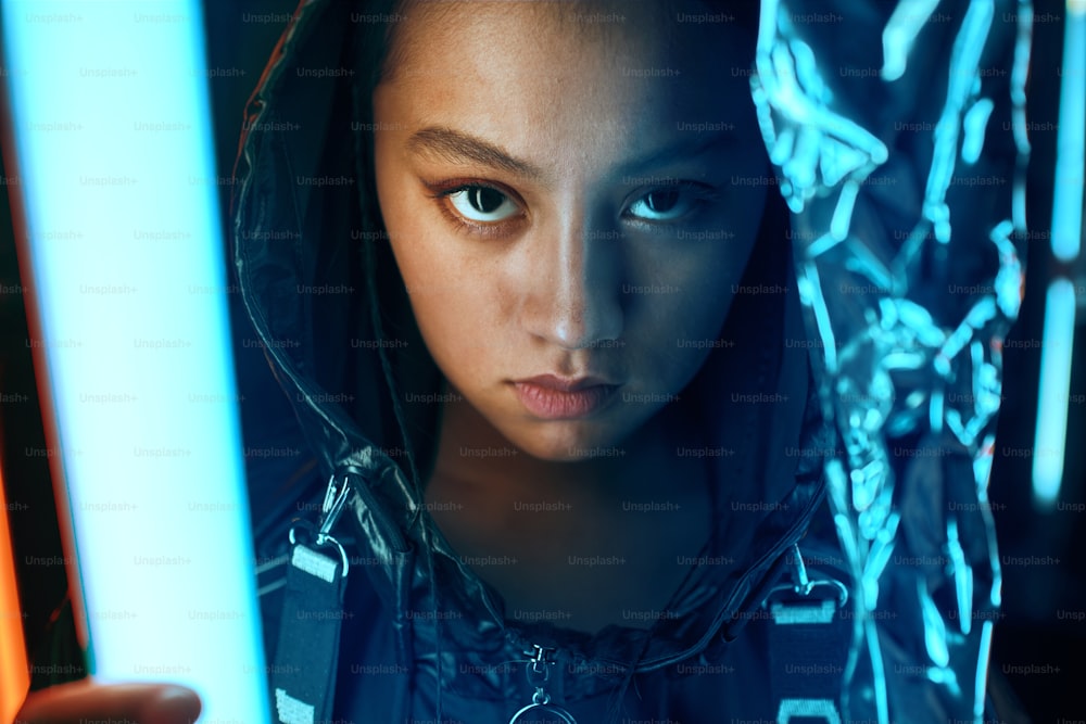 Futuristic portrait of asian teenager in neon light. She is seriour, daring, cyberpunk fashionable girl