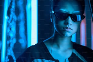 Portrait of young asian teenage girl in stylish crescent shaped sun glasses with white eyebrows, in red anf blue neon light. Cyber, futuristic portrait concept
