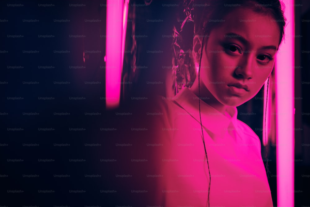 Portrait d’une jeune adolescente asiatique la main tournée vers la caméra, en néon violet. Cyber, concept de portrait futuriste