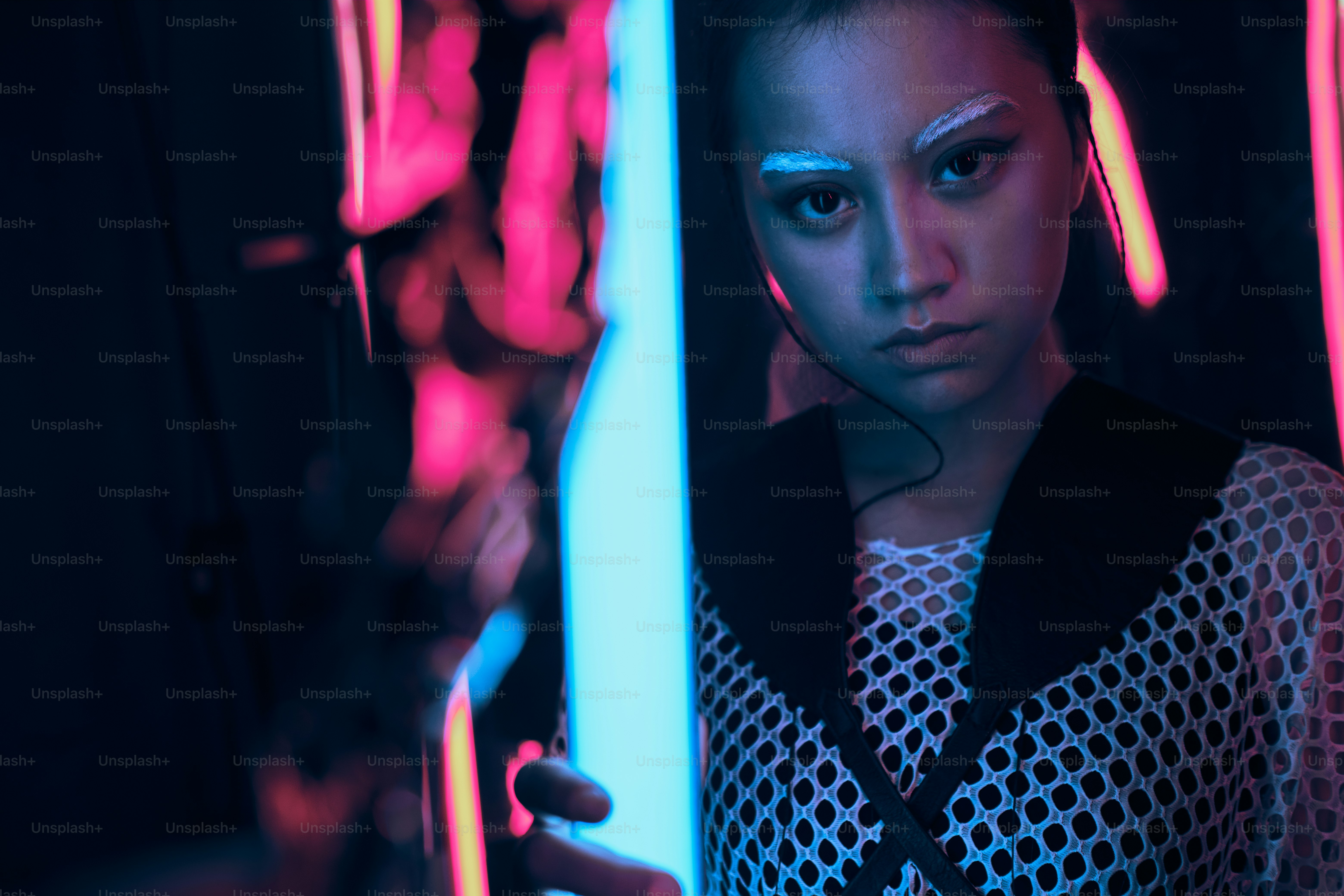 Potret futuristik remaja asia dalam cahaya neon memegang pedang seperti lampu. Dia adalah gadis modis cyberpunk yang berani, mengenakan pakaian jaring, alis putih