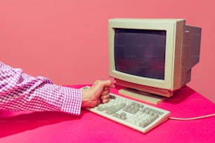 Image colorée d’un écran d’ordinateur et d’un clavier vintage isolés sur un fond rose vif. Concept de pop art rétro, de choses vintage, mélange d’ancien et de modernité. Espace de copie pour l’annonce